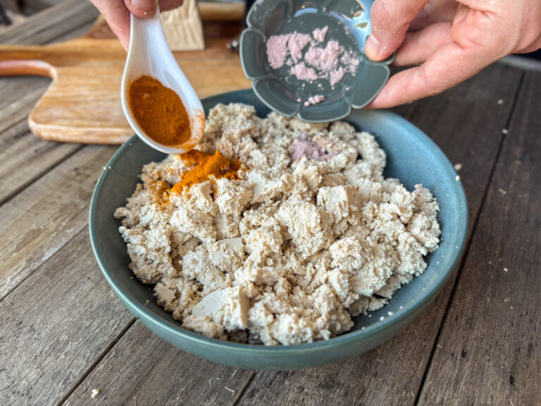 Image of bowl of crumbled tofu while adding in turmeric and black salt.